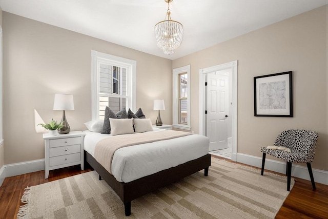 bedroom featuring an inviting chandelier, baseboards, and wood finished floors