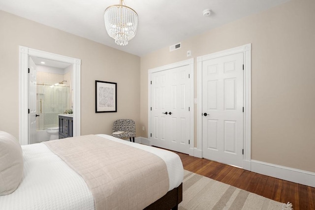 bedroom featuring visible vents, an inviting chandelier, wood finished floors, baseboards, and ensuite bathroom