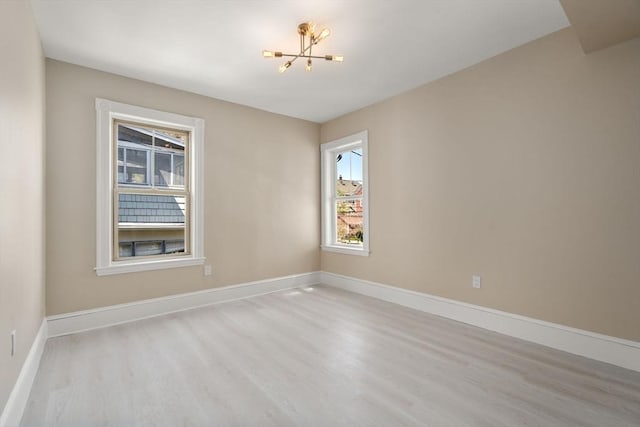empty room with baseboards, wood finished floors, a notable chandelier, and a healthy amount of sunlight