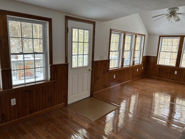 doorway to outside featuring ceiling fan, wood walls, a textured ceiling, lofted ceiling, and hardwood / wood-style flooring