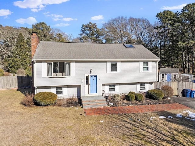 raised ranch with roof with shingles, a chimney, a front yard, and fence