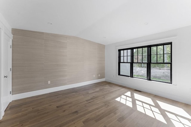 spare room featuring wood-type flooring and vaulted ceiling