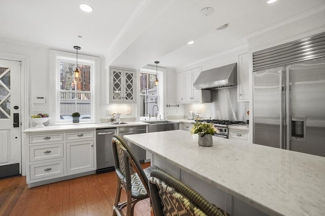 kitchen featuring premium appliances, a sink, light stone countertops, wall chimney exhaust hood, and a kitchen bar