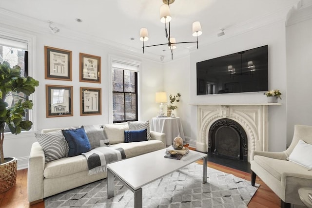 living area with ornamental molding, a notable chandelier, a fireplace with flush hearth, and wood finished floors