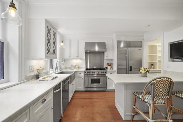 kitchen with a sink, wall chimney exhaust hood, white cabinets, and premium appliances