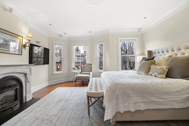 bedroom featuring a fireplace with flush hearth, multiple windows, wood finished floors, and crown molding