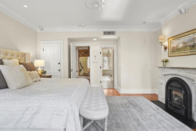 bedroom featuring a fireplace, visible vents, wood finished floors, and ornamental molding