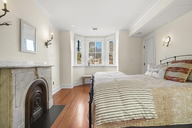 bedroom with visible vents, hardwood / wood-style floors, ornamental molding, a fireplace with flush hearth, and baseboards