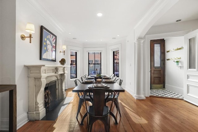 dining area featuring ornate columns, a fireplace with flush hearth, light wood-style floors, ornamental molding, and baseboards