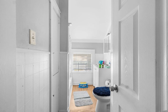 bathroom with toilet, tile walls, wood-type flooring, and ornamental molding