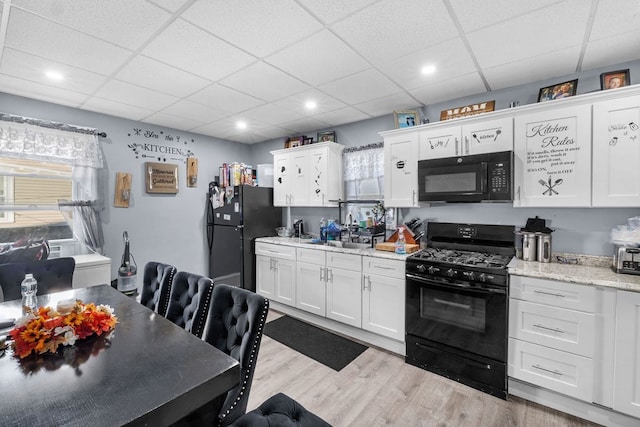 kitchen with white cabinets, light stone countertops, black appliances, and light wood-type flooring