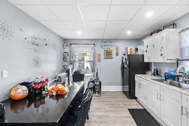 kitchen featuring light hardwood / wood-style floors, white cabinetry, sink, a paneled ceiling, and black refrigerator