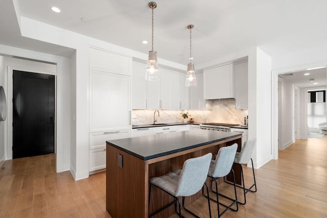 kitchen with a sink, light wood-style floors, dark countertops, and a center island