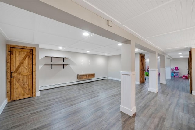 basement with a baseboard heating unit, hardwood / wood-style flooring, and a barn door