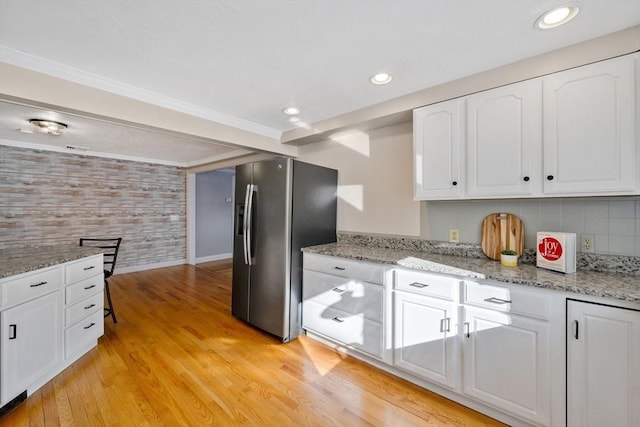 kitchen featuring white cabinetry, crown molding, stainless steel fridge, light stone countertops, and light hardwood / wood-style floors