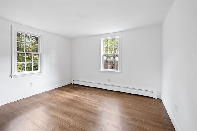 empty room featuring a baseboard heating unit, hardwood / wood-style floors, and a wealth of natural light