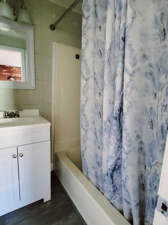 bathroom with wood finished floors, shower / bath combination with curtain, vanity, and tile walls