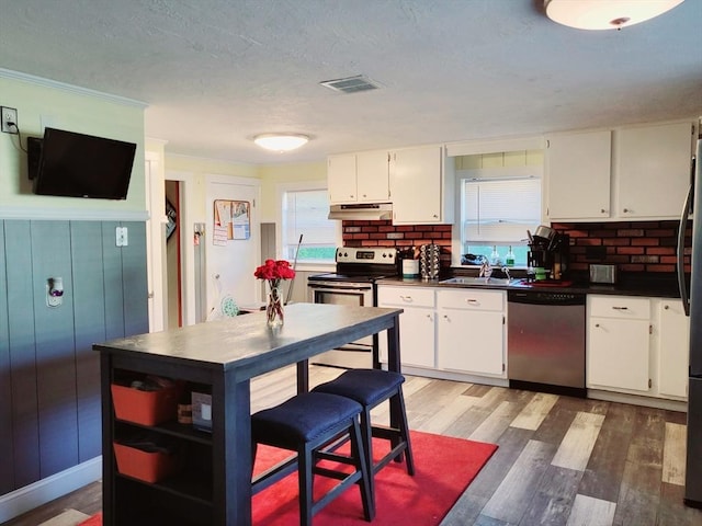kitchen featuring stainless steel appliances, under cabinet range hood, dark countertops, healthy amount of natural light, and a textured ceiling