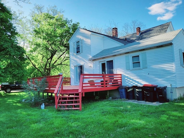 back of house with a chimney, a deck, a lawn, and roof with shingles