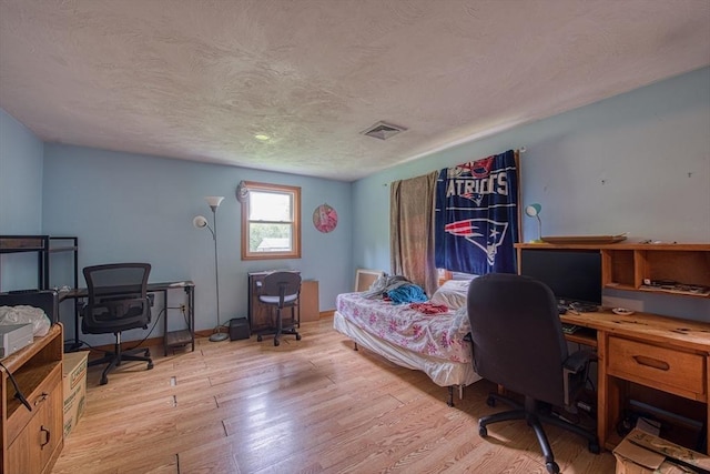 bedroom featuring a desk, light wood-style floors, and a textured ceiling