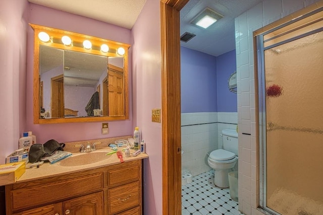 full bath featuring a stall shower, tile walls, vanity, tile patterned flooring, and toilet
