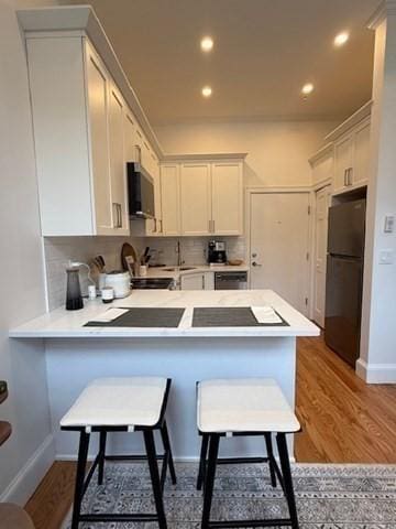 kitchen with freestanding refrigerator, a peninsula, light countertops, a sink, and backsplash