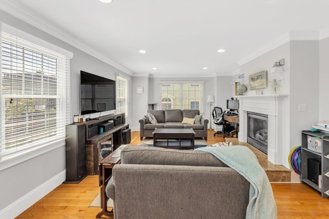 living room with light wood-style flooring, a glass covered fireplace, recessed lighting, crown molding, and baseboards