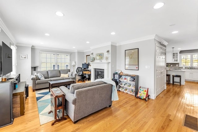 living area featuring recessed lighting, light wood finished floors, a glass covered fireplace, and crown molding