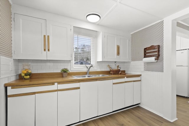 63 Adams St, Bourne, MA 02532 - kitchen with a sink, white cabinetry, decorative backsplash, white fridge, and wood finished floors