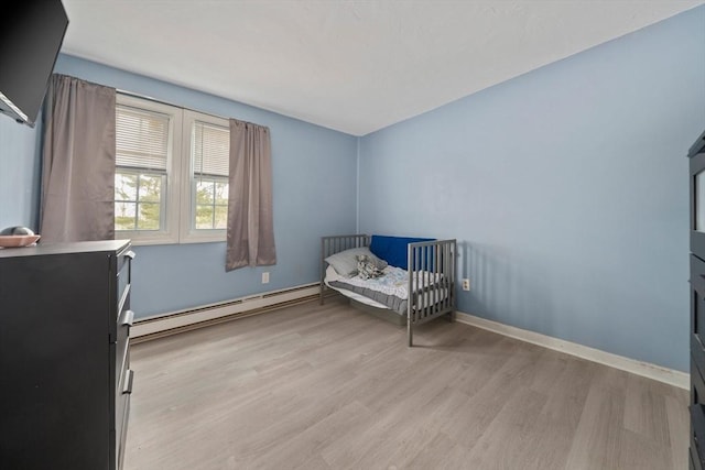 bedroom featuring light wood-type flooring, a baseboard heating unit, and baseboards