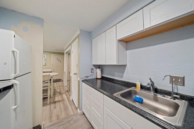 kitchen with light wood-style flooring, freestanding refrigerator, a sink, white cabinets, and dark countertops