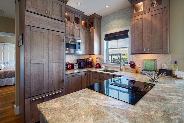 kitchen featuring sink, hardwood / wood-style flooring, built in appliances, light stone countertops, and decorative backsplash