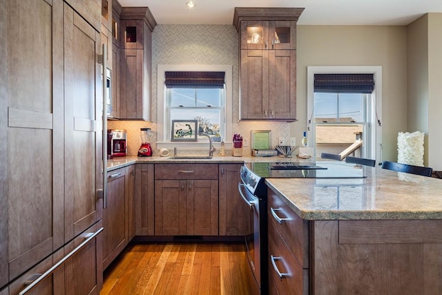 kitchen with sink, light stone counters, stainless steel electric range oven, light wood-type flooring, and backsplash