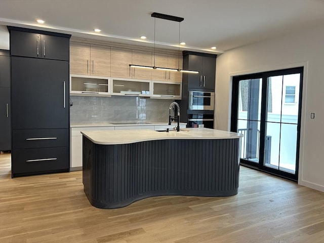 kitchen with pendant lighting, sink, an island with sink, and light hardwood / wood-style flooring