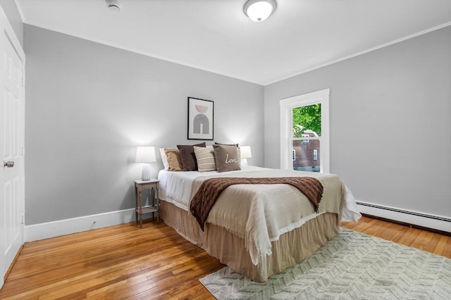 bedroom with hardwood / wood-style floors, baseboards, crown molding, and a baseboard heating unit