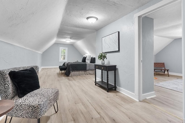 bedroom with vaulted ceiling, wood finished floors, a textured ceiling, baseboards, and a textured wall