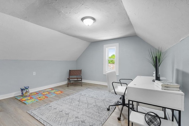 office space with wood finished floors, vaulted ceiling, baseboards, and a textured ceiling