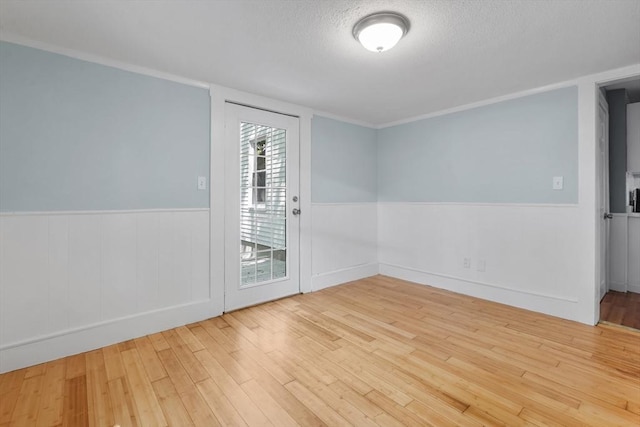 spare room with wood finished floors, wainscoting, and a textured ceiling