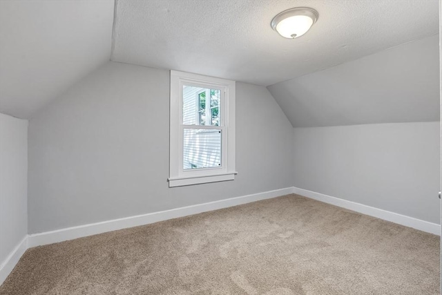 additional living space with carpet floors, baseboards, lofted ceiling, and a textured ceiling