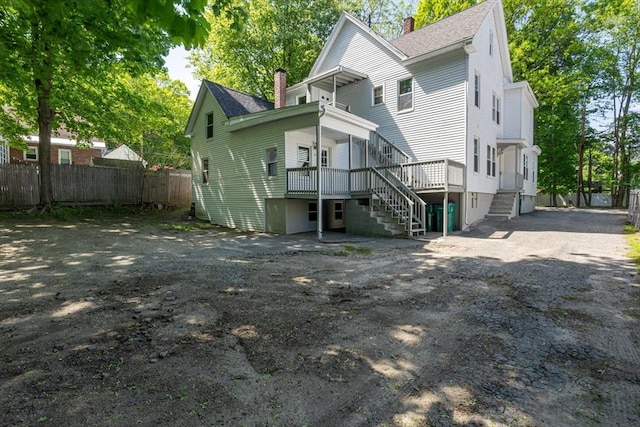 rear view of house with a chimney, stairway, fence, a shingled roof, and asphalt driveway