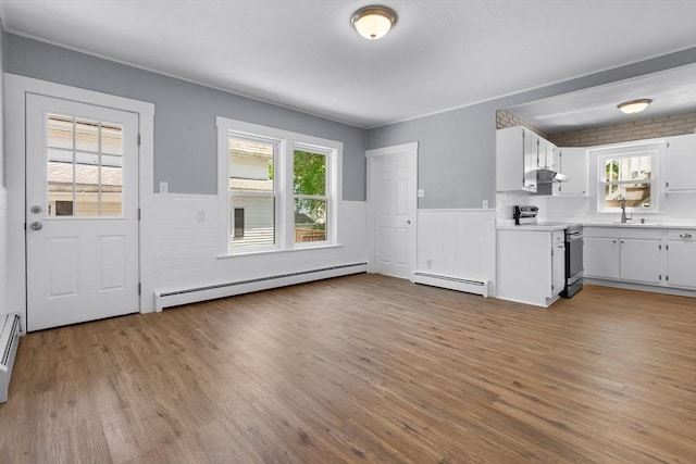 kitchen with stainless steel range with electric cooktop, baseboard heating, wainscoting, light countertops, and a sink
