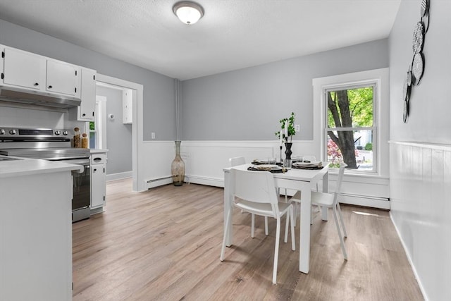dining area with light wood finished floors, a baseboard radiator, a textured ceiling, and a wainscoted wall