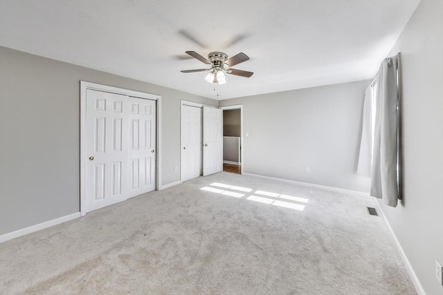 unfurnished bedroom featuring ceiling fan, light colored carpet, and two closets