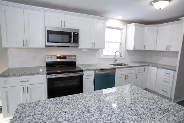 kitchen with white cabinets, decorative backsplash, light stone countertops, stainless steel appliances, and a sink