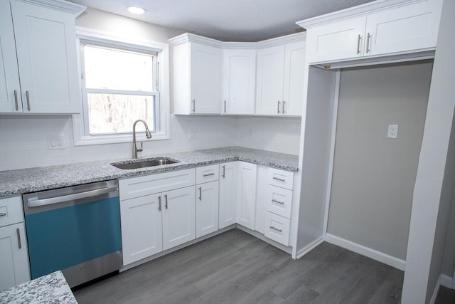 kitchen with light stone counters, white cabinetry, a sink, wood finished floors, and dishwashing machine