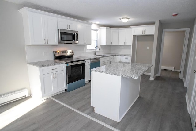 kitchen featuring appliances with stainless steel finishes, light stone counters, light wood-type flooring, white cabinetry, and a sink