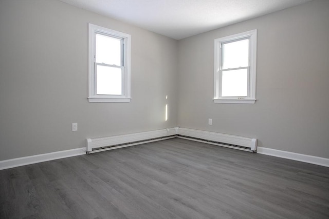 empty room with a healthy amount of sunlight, a baseboard radiator, baseboards, and dark wood finished floors