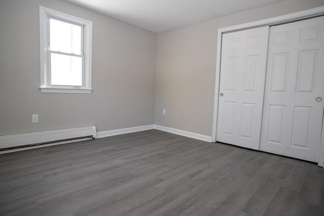 unfurnished bedroom featuring a baseboard radiator, a closet, dark wood finished floors, and baseboards