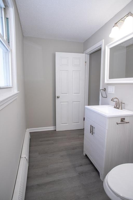 bathroom with toilet, wood finished floors, baseboard heating, a textured ceiling, and vanity