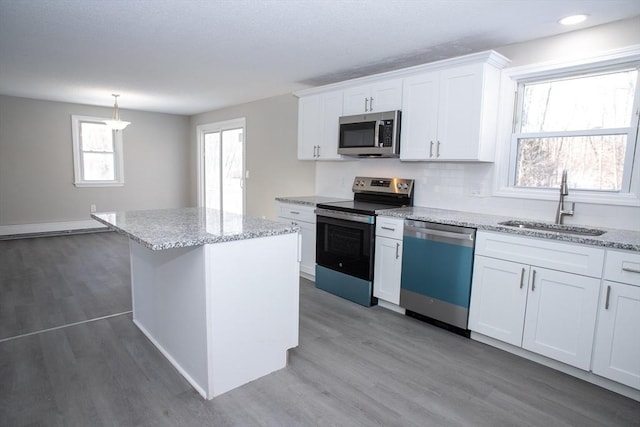 kitchen with a center island, stainless steel appliances, white cabinets, a sink, and wood finished floors